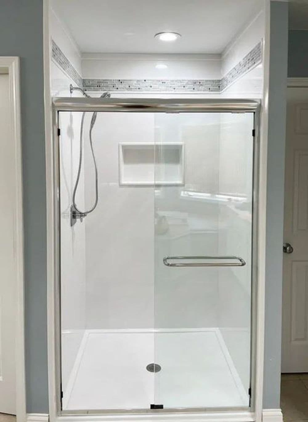 Modern walk-in shower with glass door, white tiles, and brushed nickel fixtures.