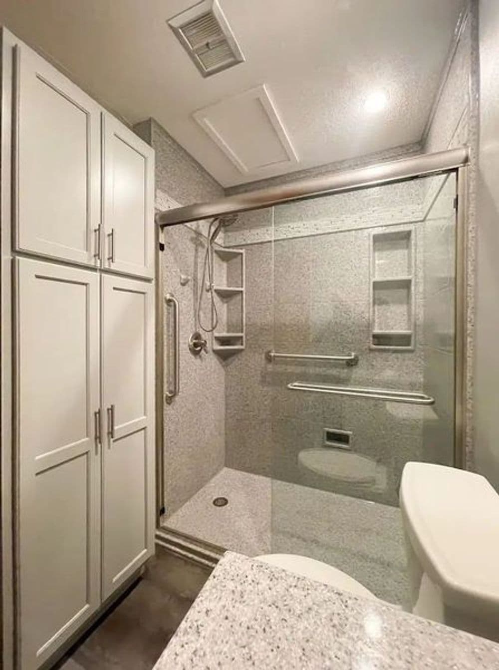 Modern bathroom featuring a glass shower, granite countertop, and ample storage cabinets.