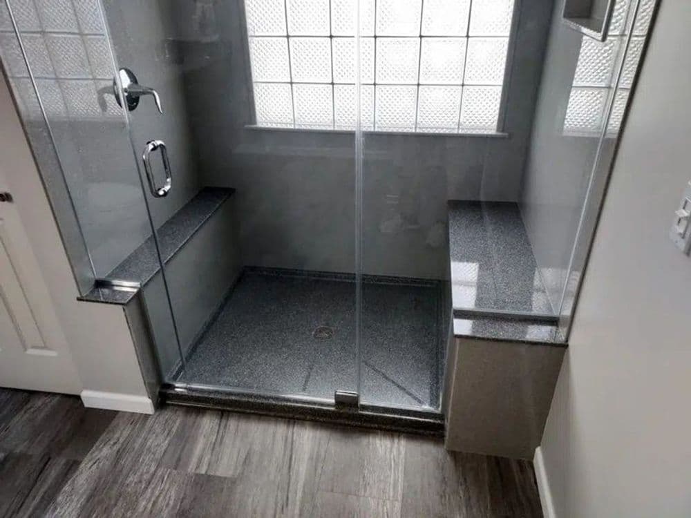 Modern glass shower with gray stone accents and seating in a well-lit bathroom.