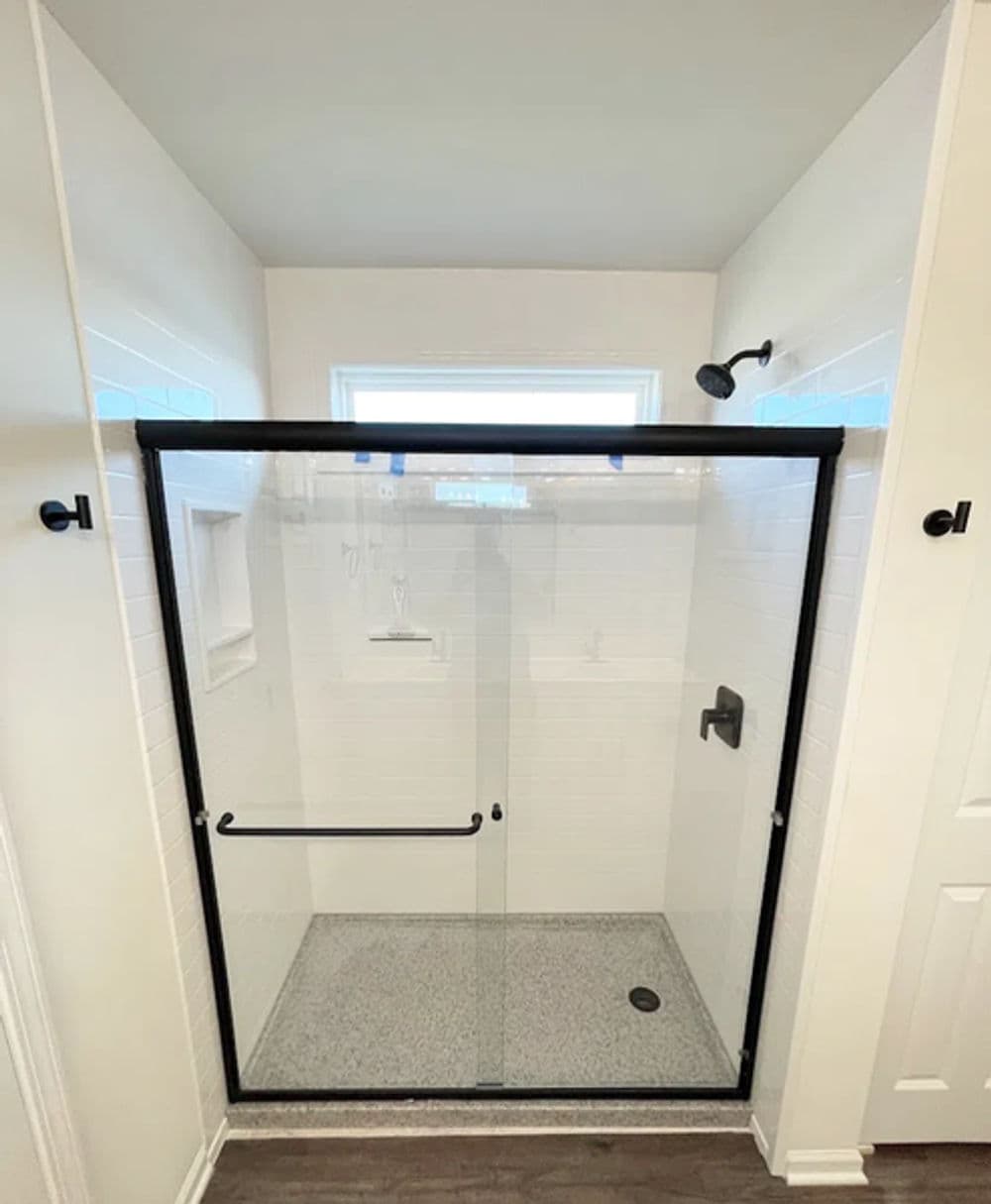 Modern shower enclosure with black frame, minimalist design, and textured flooring.