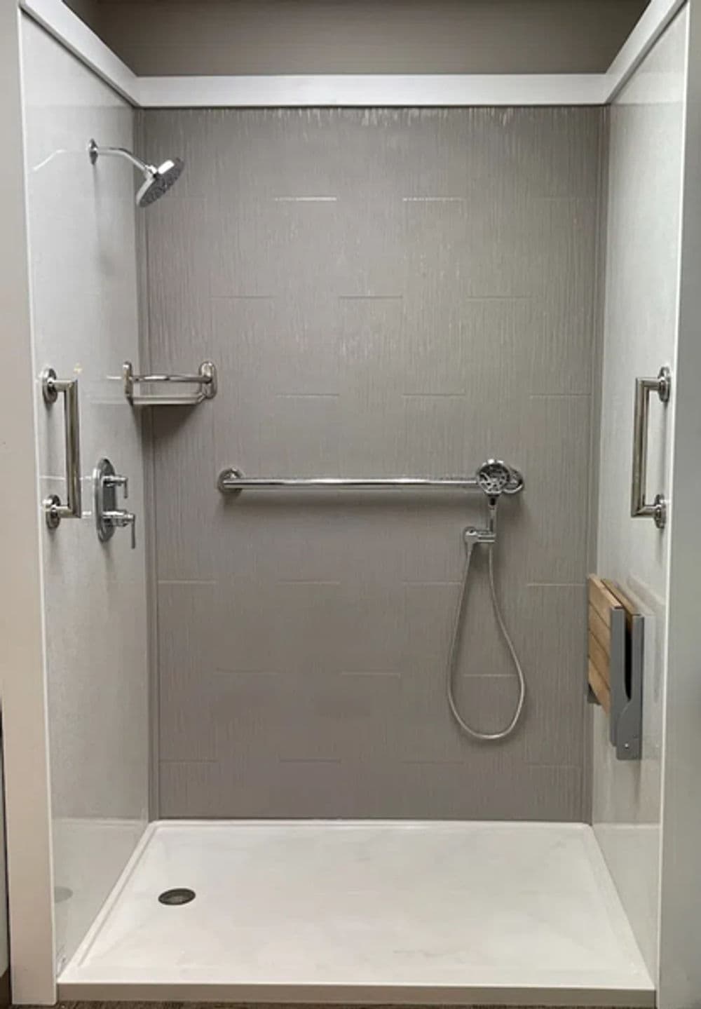 Accessible walk-in shower with grab bars, handheld showerhead, and minimalistic design.