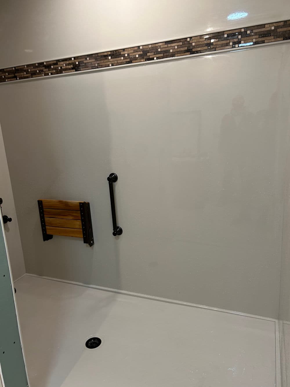 Accessible modern shower with grab bars and a foldable bench, featuring stylish tile accents.