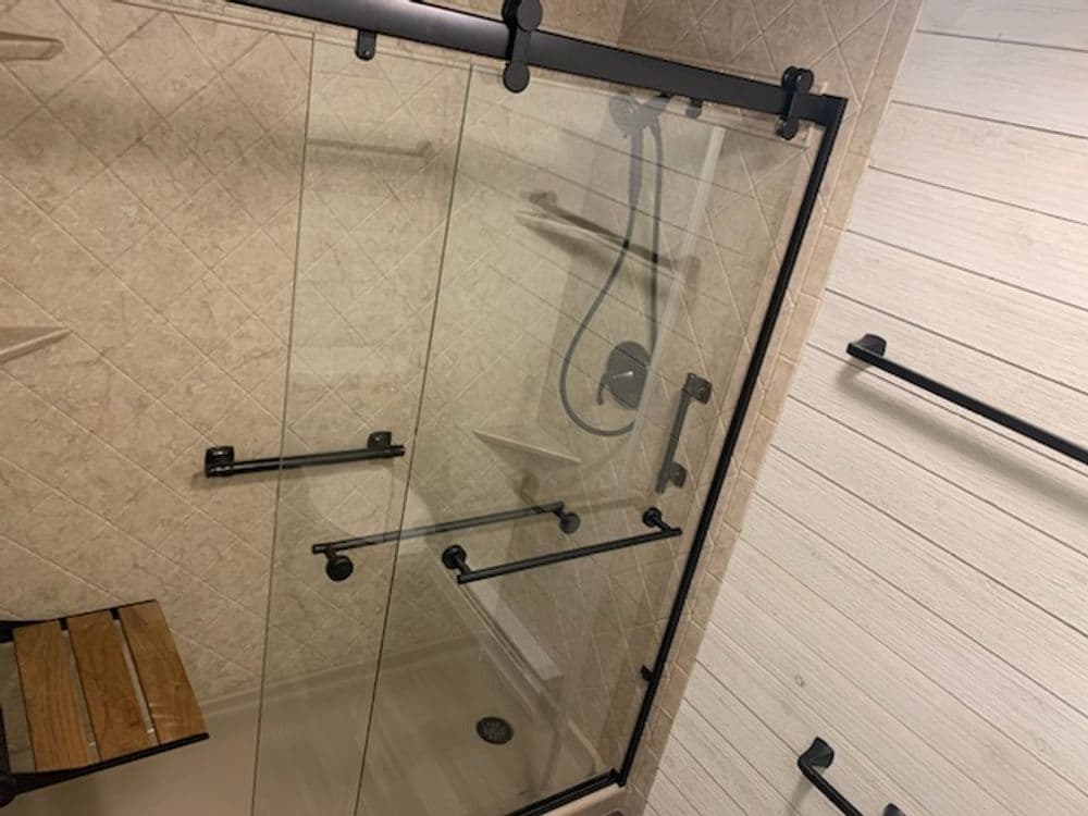 Modern glass shower enclosure with black metal accents and wooden bench in a tiled bathroom.