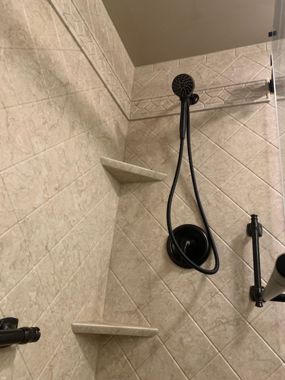 Modern shower with a handheld showerhead and built-in stone shelves on tiled walls.