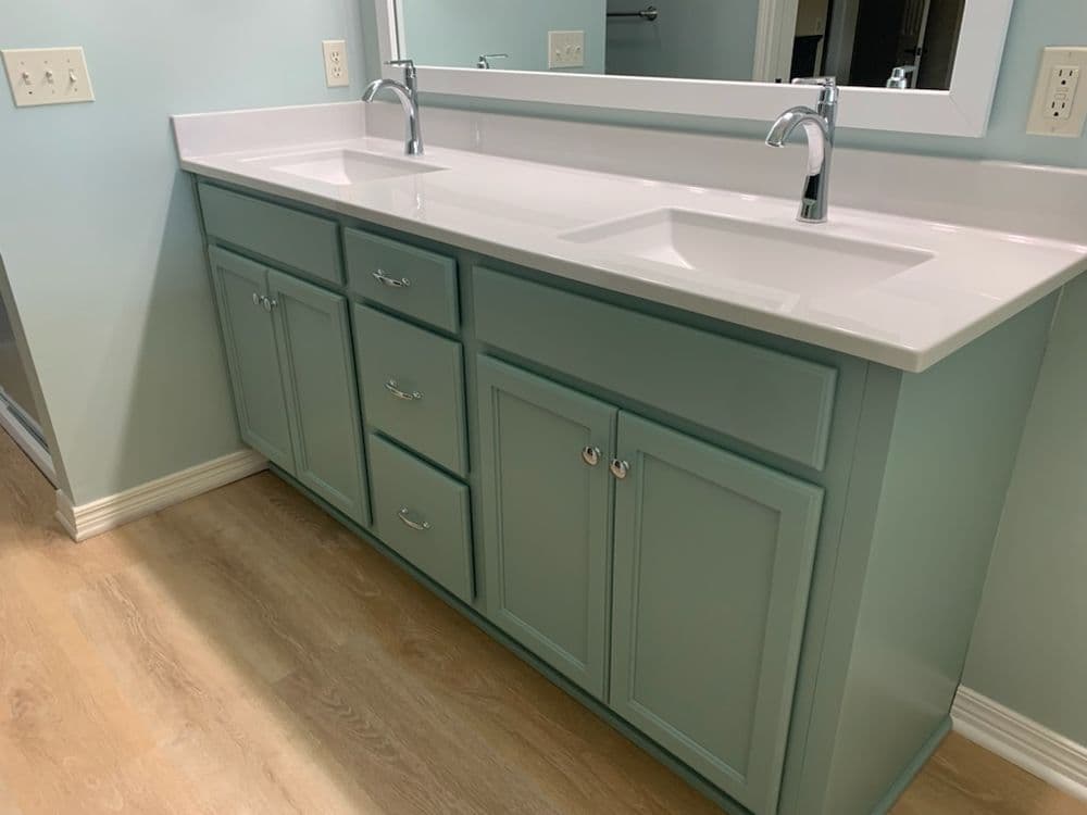 Modern bathroom vanity in soft teal with dual sinks and ample storage drawers.