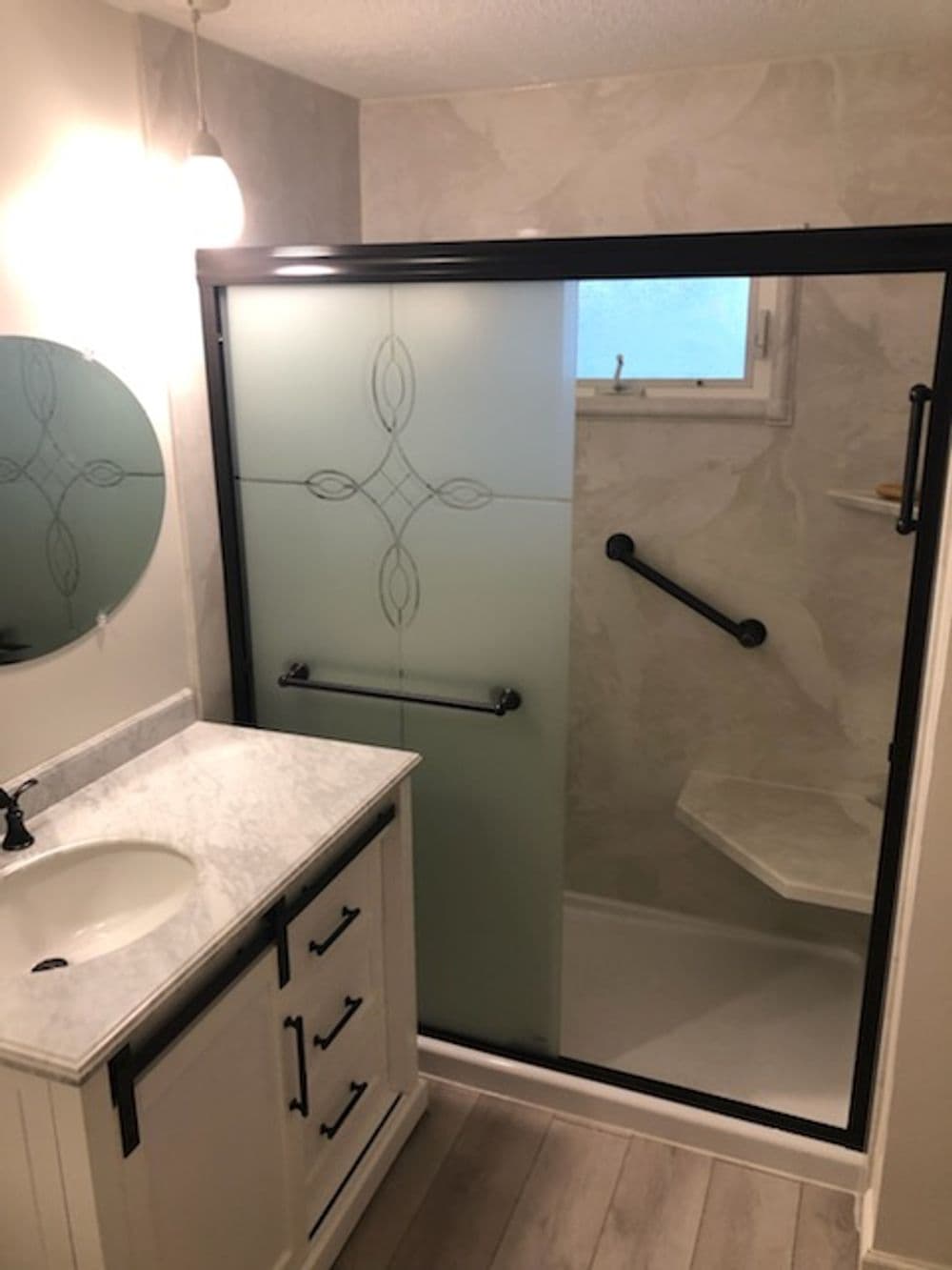 Modern bathroom with frosted glass shower, marble countertop, and sleek black accents.