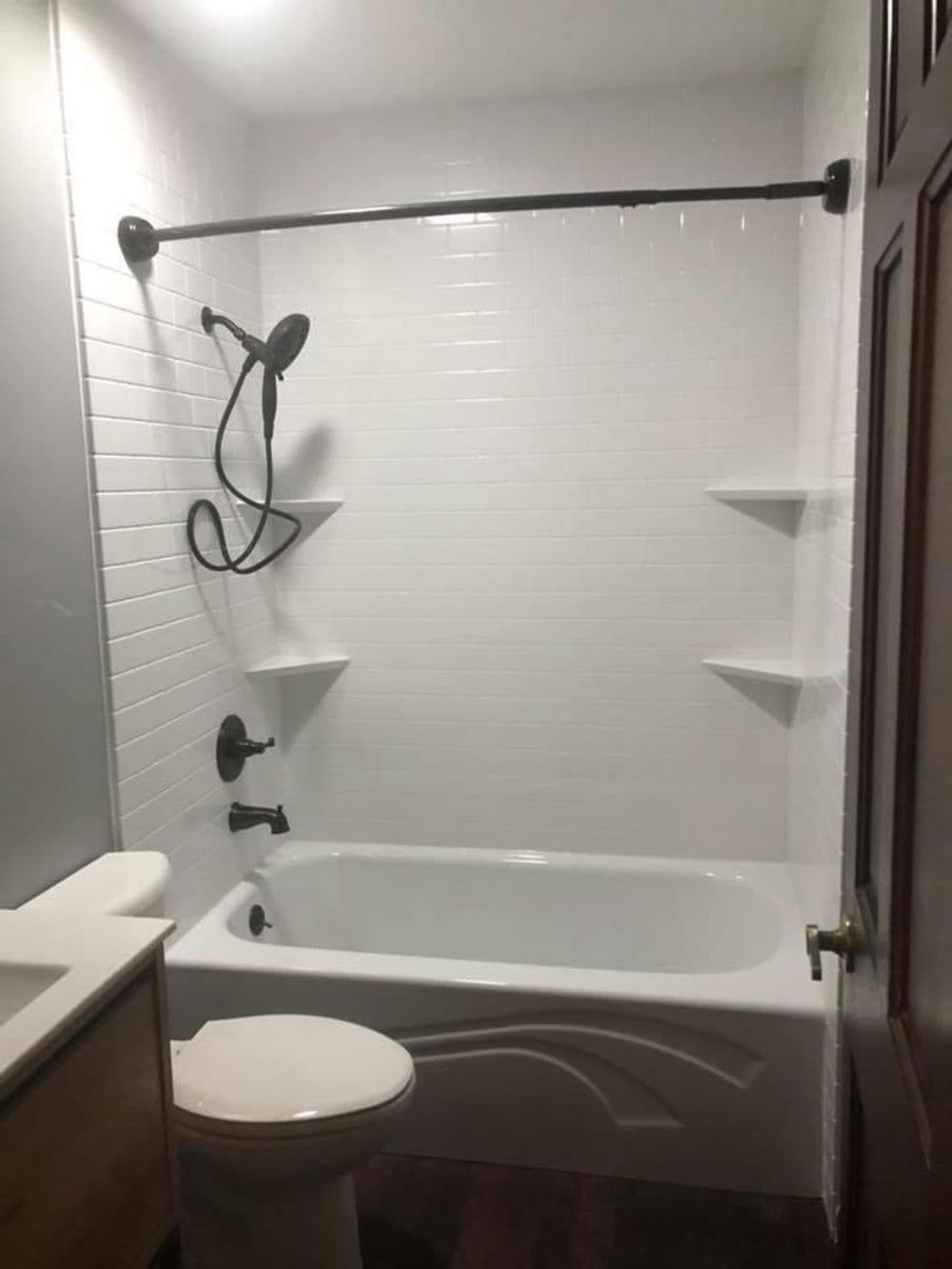 Modern bathroom with white tiled walls, showerhead, bathtub, and minimalist shelving.