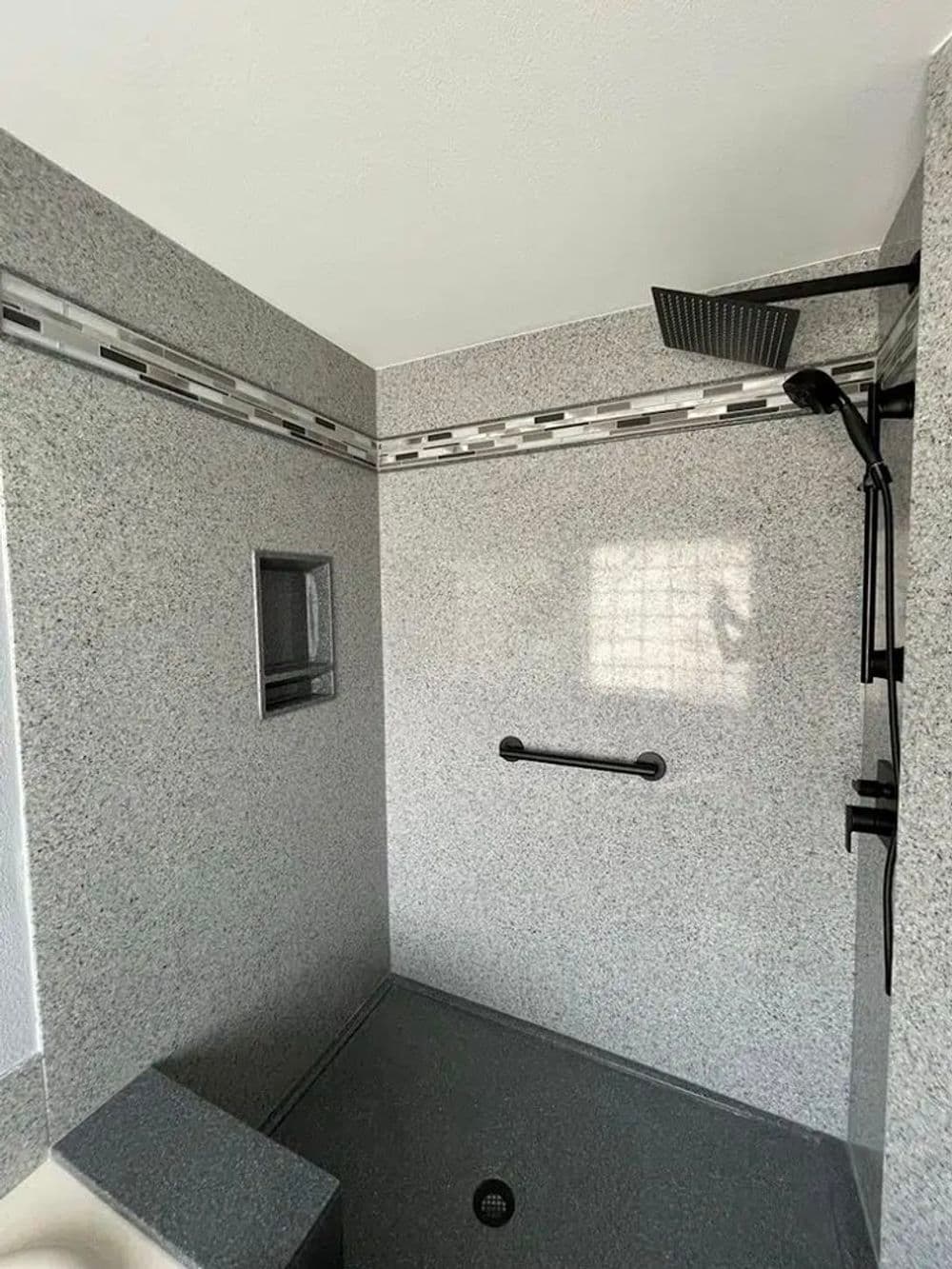 Modern shower with sleek gray tiles, overhead showerhead, and grab bar for safety.