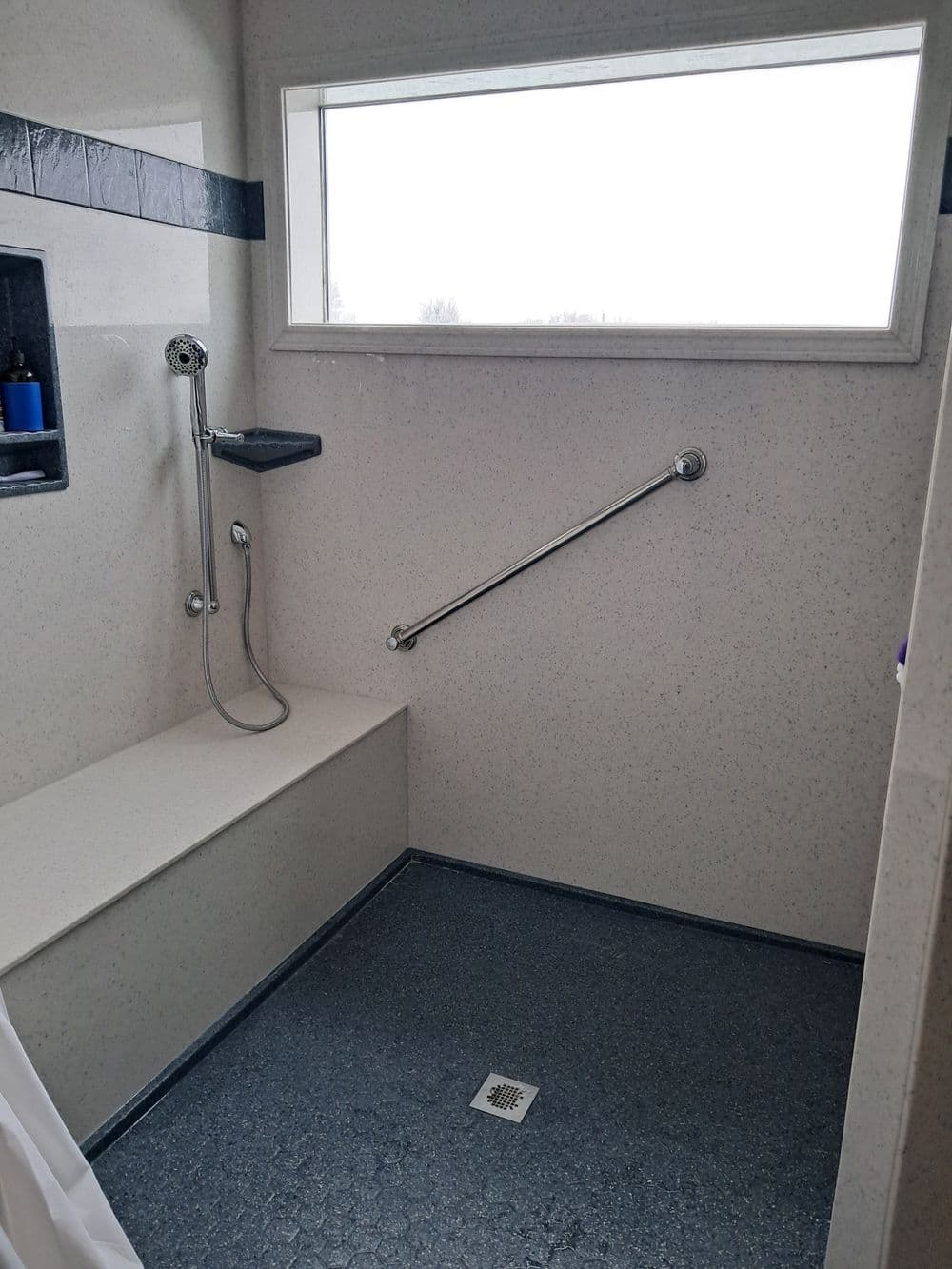 Modern accessible shower featuring a grab bar, handheld showerhead, and a built-in bench.