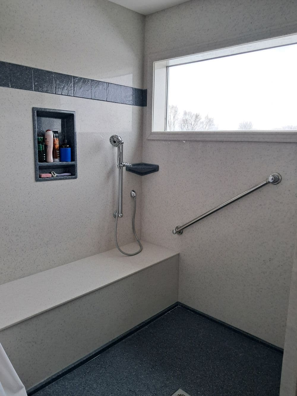 Accessible modern shower with safety grab bars, built-in shelf, and large window for natural light.