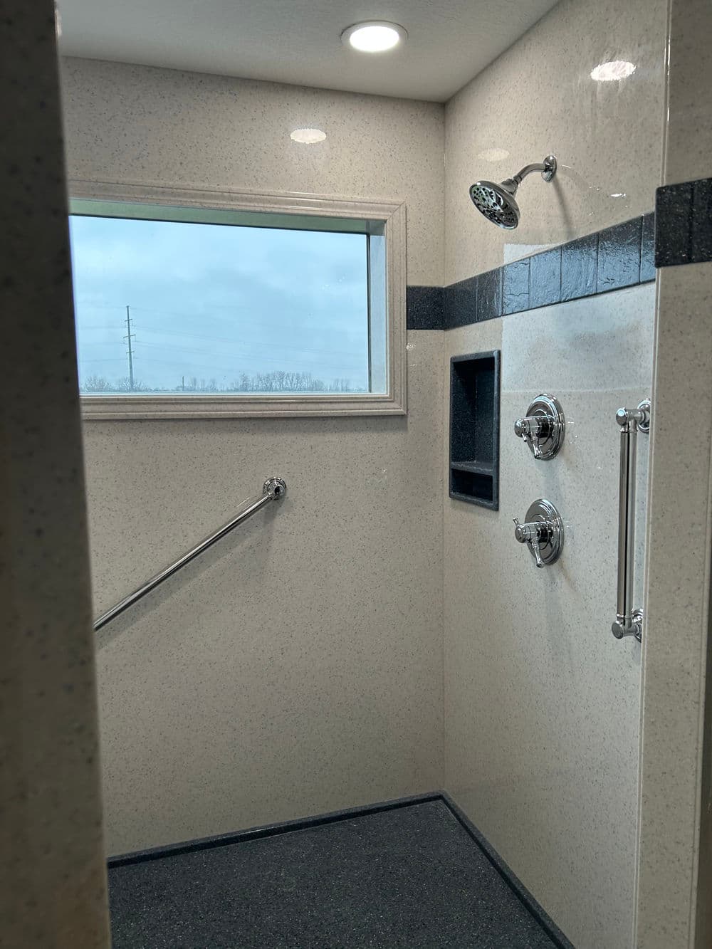 Modern shower design featuring a window, chrome fixtures, grab bars, and textured walls.