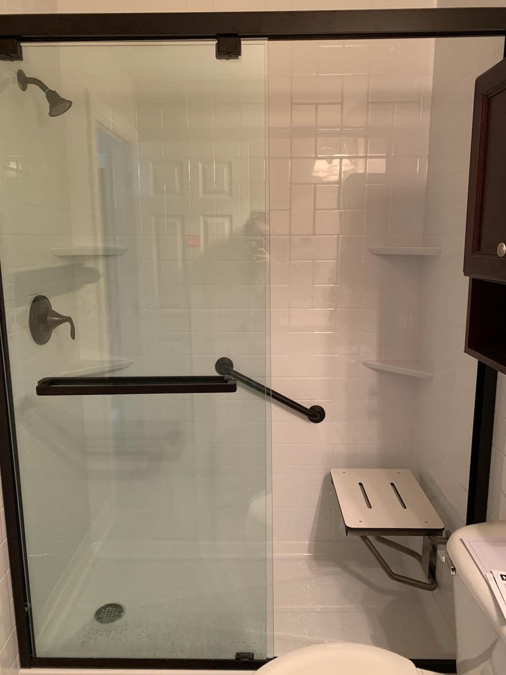Modern walk-in shower with glass door, grab bars, and built-in shelving for accessibility.